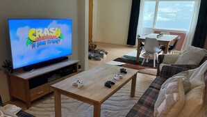 A living room with a television displaying a game, a coffee table with gaming controllers, a sofa, and a view of the outdoors through a window. - Solvang Ferienhaus mit Fjordblick & privatem Garten (Møre og Romsdal)