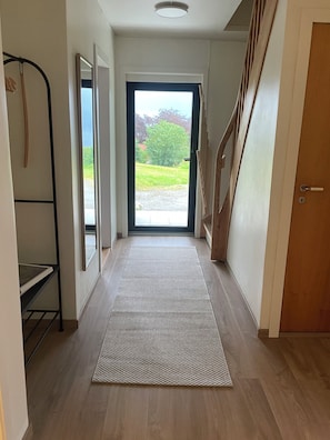 A hallway with a wooden floor, a patterned rug, a metal rack, and a view of the outdoors through a glass door.