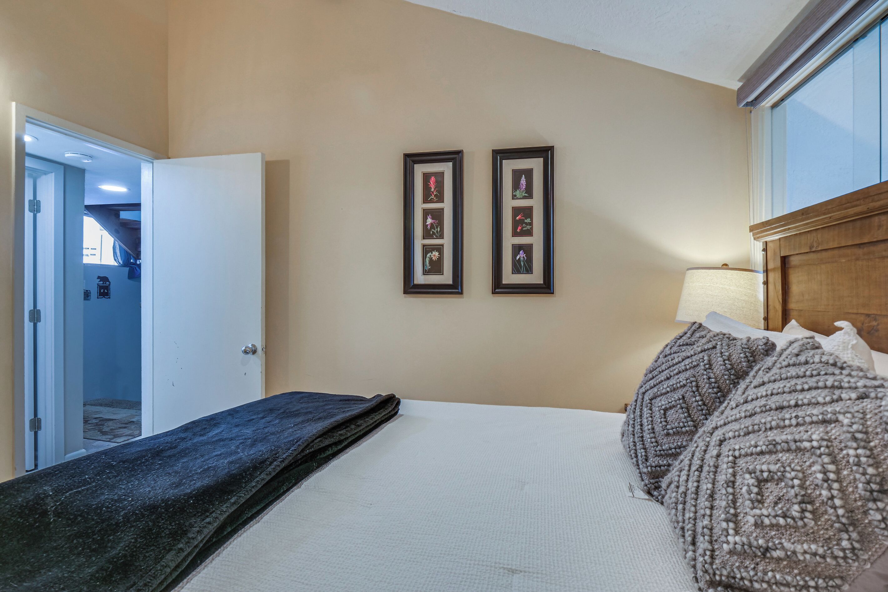 A hotel room with a bed, a nightstand, a lamp, and two framed pictures on the wall.