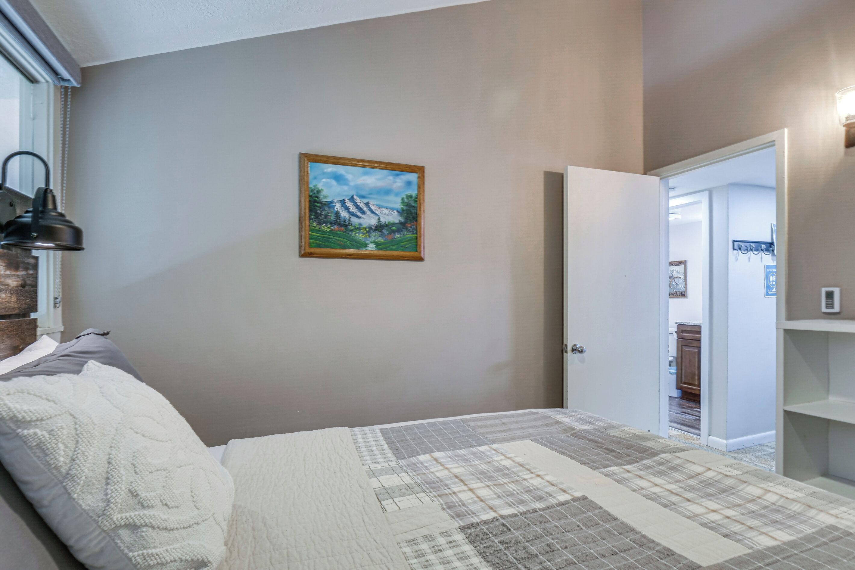 Een slaapkamer met een bed, een schilderij aan de muur en een deur naar een andere kamer.