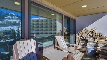 A balcony with two Adirondack chairs, a stack of firewood, and a view of a mountain resort.