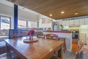 A cozy kitchen with wooden cabinets, a dining table with chairs, and a view of a snowy landscape through large windows.