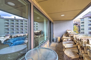 Ein Balkon mit Glastür, Tisch und Stuhl. Holzscheite und ein Metalleimer sind gestapelt.