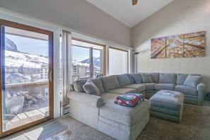 A living room with a sectional sofa, a coffee table, and a painting on the wall. - Snowcrest Condo | Walk to the Lifts (crested butte)