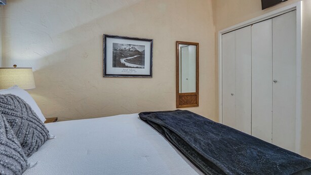 Ein Schlafzimmer mit einem Bett, einem gerahmten Bild an der Wand, einem Spiegel und einem Kleiderschrank.