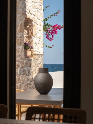 Un mur de pierres, un vase et des plantes en pot, une vue sur la mer et une table avec des chaises.