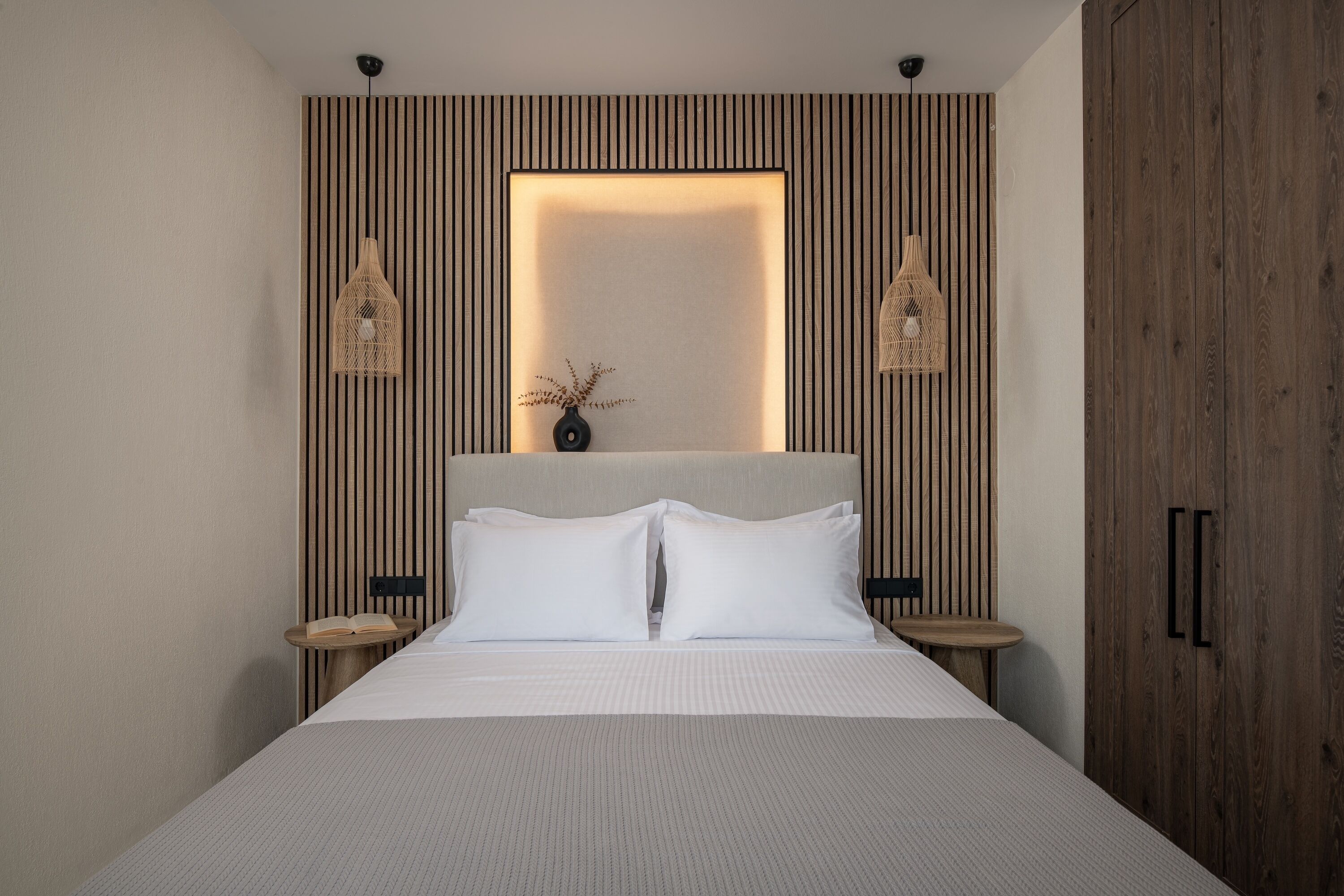Una camera da letto moderna con un letto grande, una testiera in legno a listelli verticali, due comodini con lampade e un tavolino con un libro.