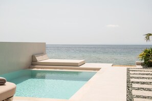 Un espace piscine avec vue sur la mer, un coin salon avec des coussins et une petite plante.