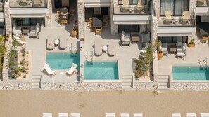 A rooftop pool area with multiple lounge chairs and tables, surrounded by stone walls and vegetation. - Strovilla Gaia 4 Luxury Private Beachfront Villas (PSKOUDIA)