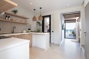 A modern kitchen with white cabinetry, a central island, and pendant lighting. - Strovilla Gaia 4 Luxury Private Beachfront Villas (PSKOUDIA)