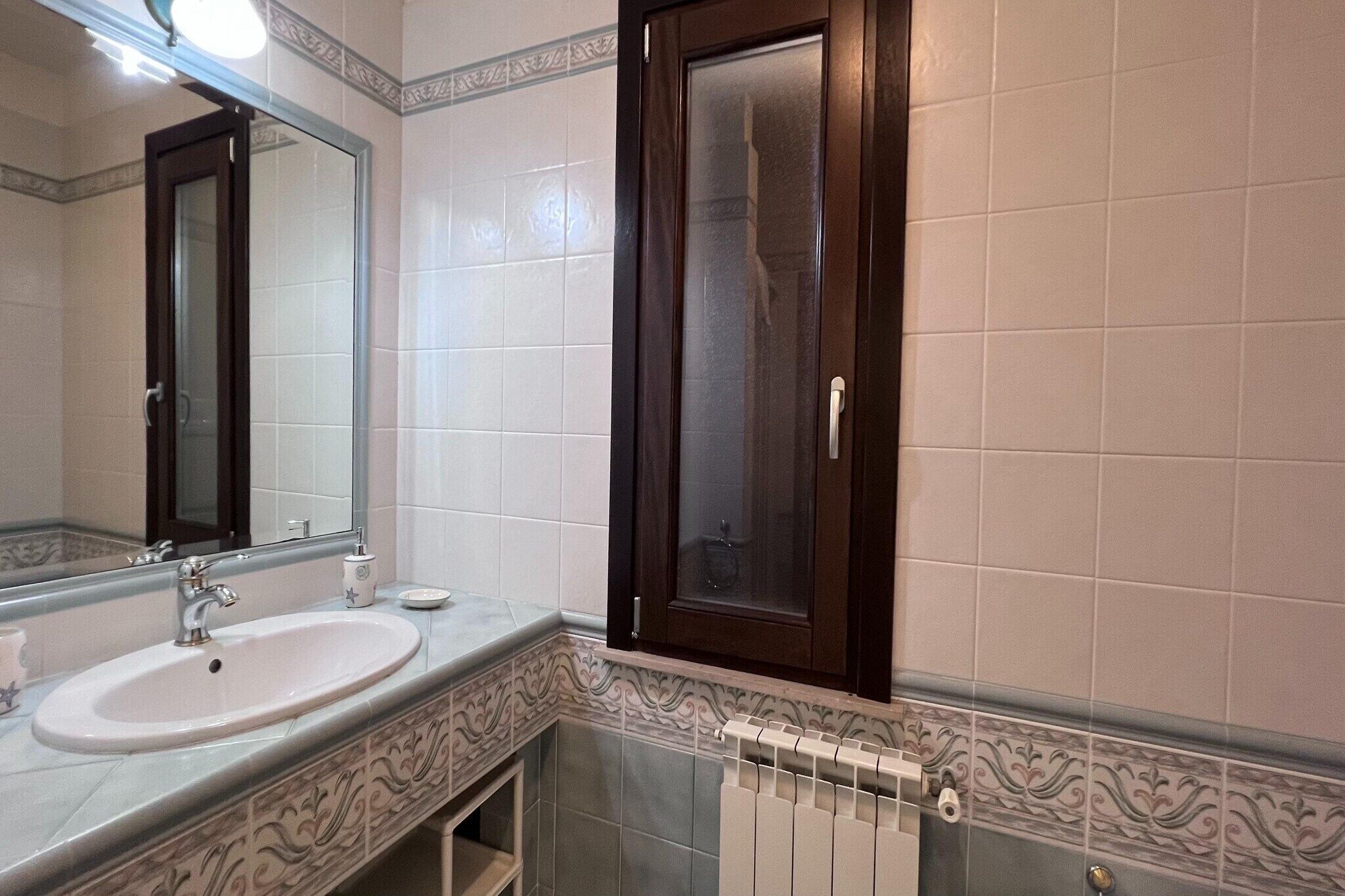 Un baño con lavamanos, espejo y un armario con puerta de vidrio.
