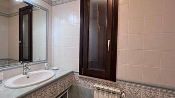 Un baño con lavamanos, espejo y un armario con puerta de vidrio.