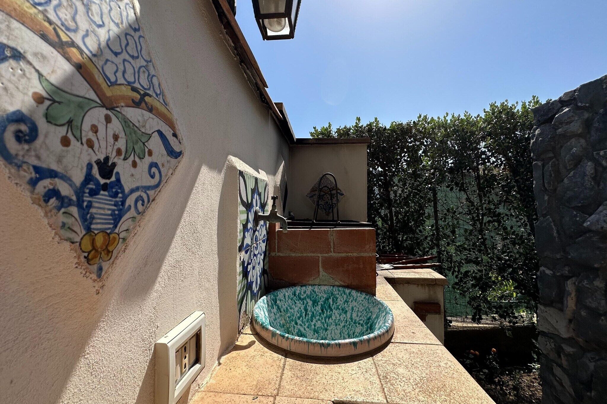 A courtyard with a tiled wall, a small pool, and a stone structure.