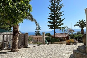 Ein mit Kopfsteinpflaster belegter Innenhof mit Blick auf das Meer, einem Tor und einem Gebäude mit Ziegeldach.