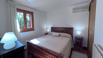 Een slaapkamer met een houten bed, een nachtkastje met lamp, een raam met gordijnen en een radiator.