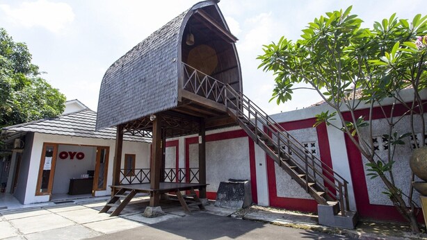 Um edifício com estrutura de telhado inclinada singular, uma escadaria que leva a um terraço, e uma pequena área externa com mesas e cadeiras.