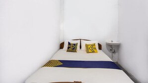 Um quarto pequeno e estreito com uma cama de solteiro, uma mesa de cabeceira e uma pia fixada na parede.