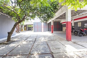 Un estacionamiento techado con un árbol, una motocicleta y un edificio de paredes rojas y blancas.