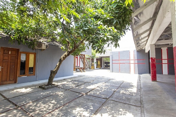 A courtyard with a tree, a building with a tiled floor, and a wall with a red and white pattern.