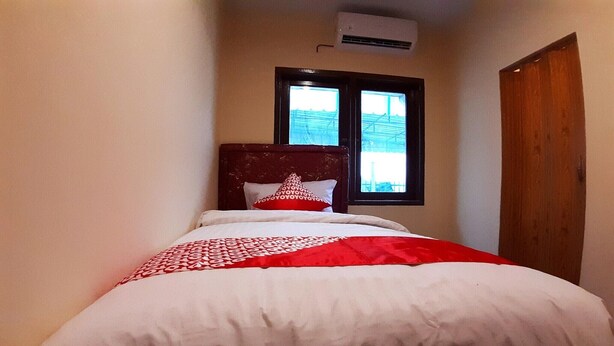A narrow hotel room with a bed, a window, and a wooden door. - Comfortable Standard Single Stay (Medan)