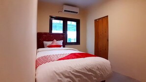 A narrow hotel room with a bed, a window, and an air conditioning unit. - Comfortable Standard Single Stay (Medan)