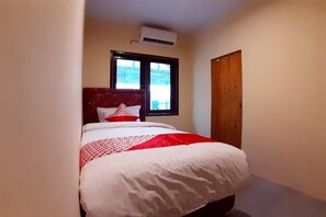 Ein schmales Hotelzimmer mit Bett, Fenster und Klimaanlage.