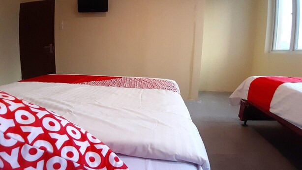 Ein Hotelzimmer mit zwei Betten, einer Tür, einem an der Wand befestigten Fernseher und einem Fenster.