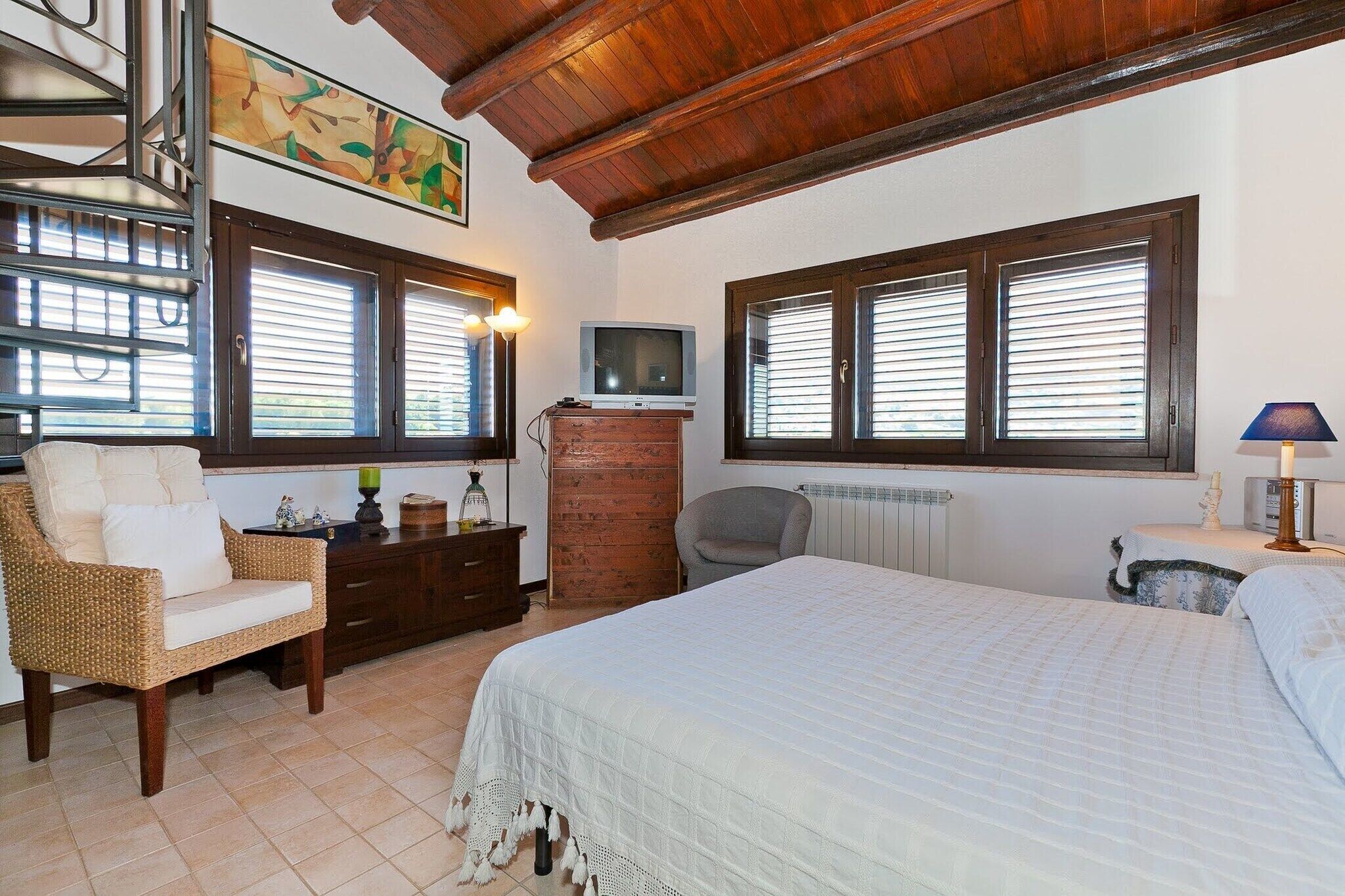 Una camera da letto con un letto, una cassettiera, una sedia, una televisione e una finestra con persiane.
