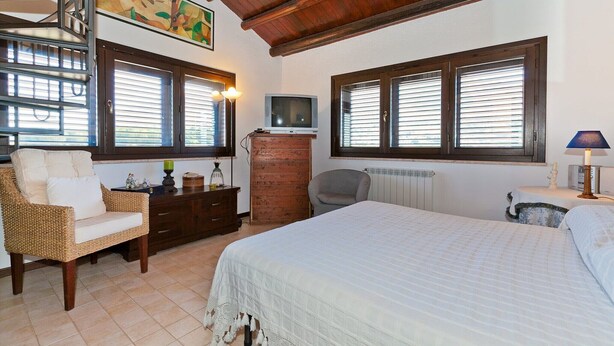 A bedroom with a bed, a dresser, a chair, a television, and a window with blinds. - Holiday Home with pool in Sicily (Castellamare del Golfo)