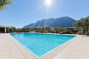 A rectangular swimming pool with clear blue water, surrounded by a tiled deck, set against a backdrop of mountains and a clear sky. - Holiday Home with pool in Sicily (Castellamare del Golfo)