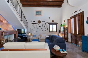 A living room with a staircase, a television, seating area, and a wall with various items. - Holiday Home with pool in Sicily (Castellamare del Golfo)