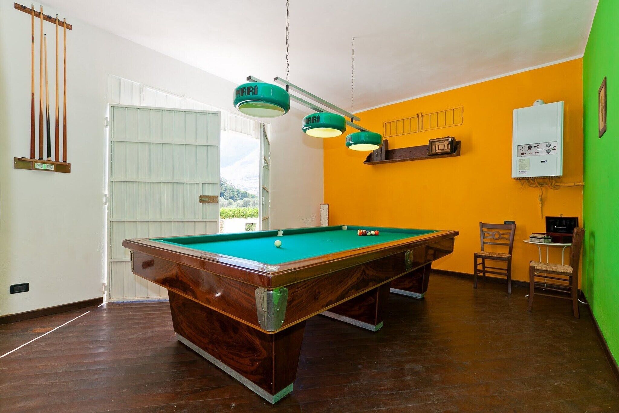 Une table de billard avec un placage en bois, un drap de jeu vert et trois lampes suspendues.