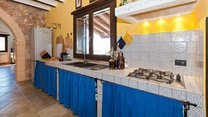 A kitchen with a stone archway, a refrigerator, a sink, a stove, and a blue tablecloth. - Holiday Home with pool in Sicily (Castellamare del Golfo)