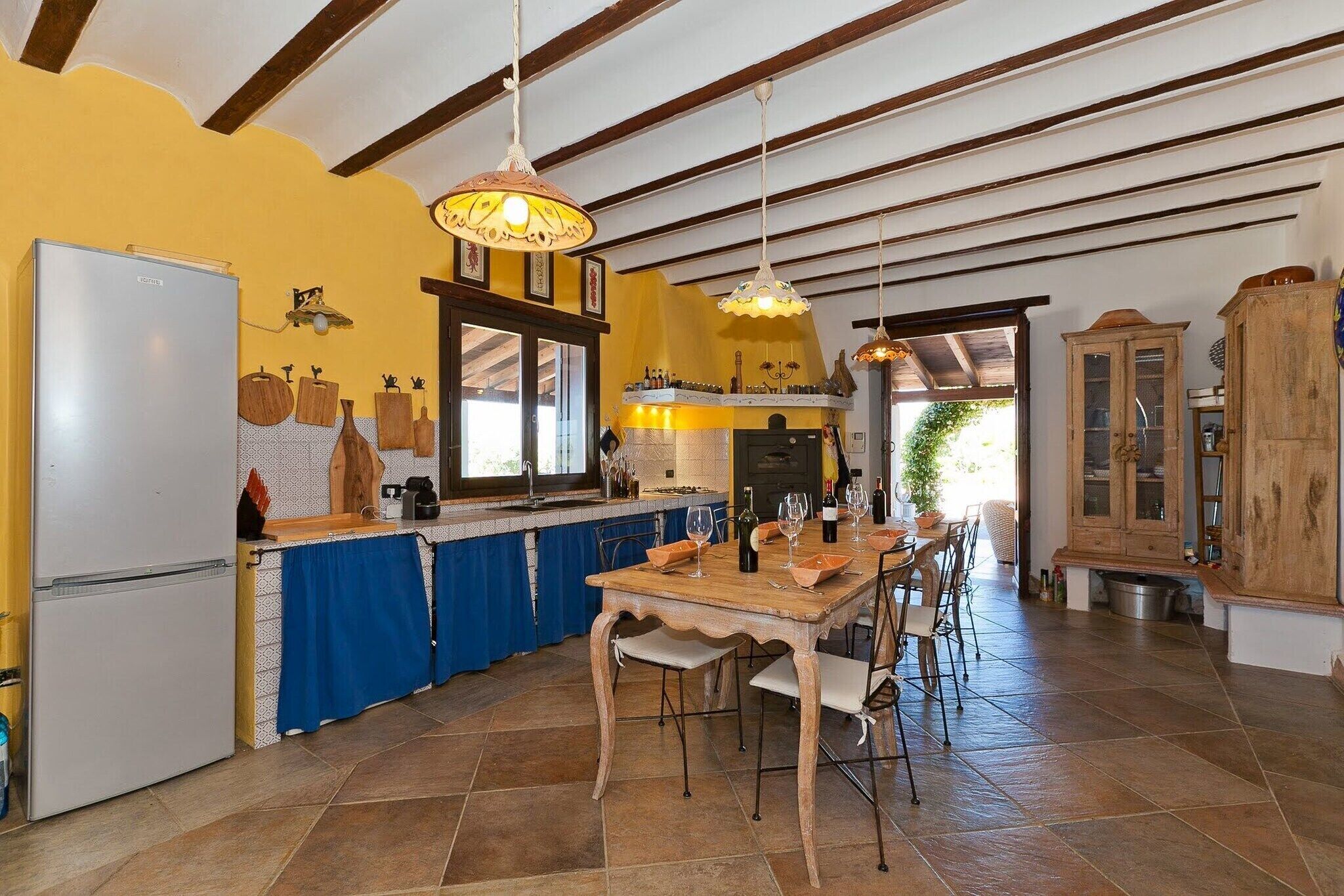 Una cucina con isola centrale, sedie di legno, tavolo da pranzo e lampade a sospensione.