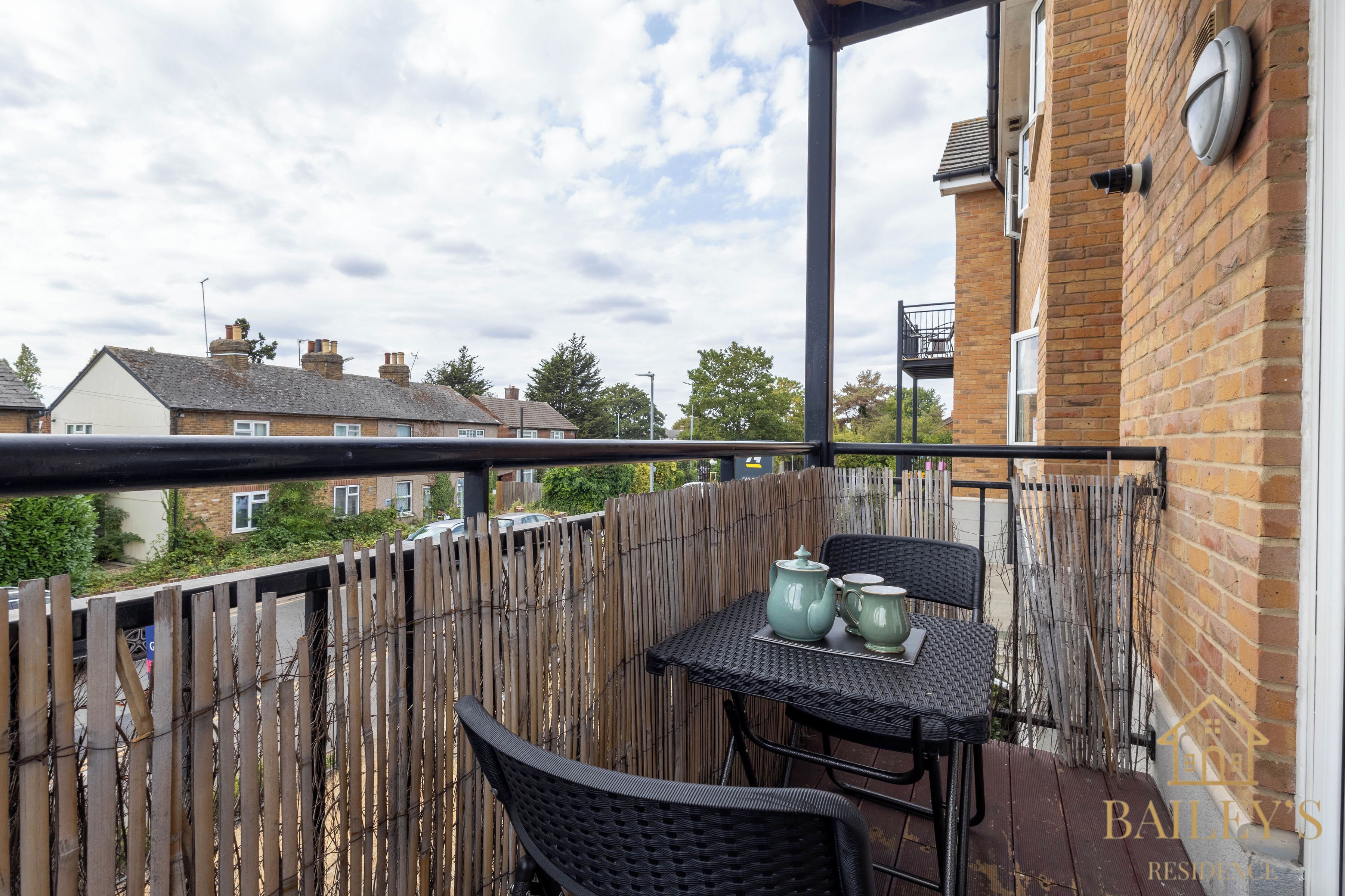Een balkon met een tafel en stoelen, een houten hek en woongebouwen op de achtergrond.
