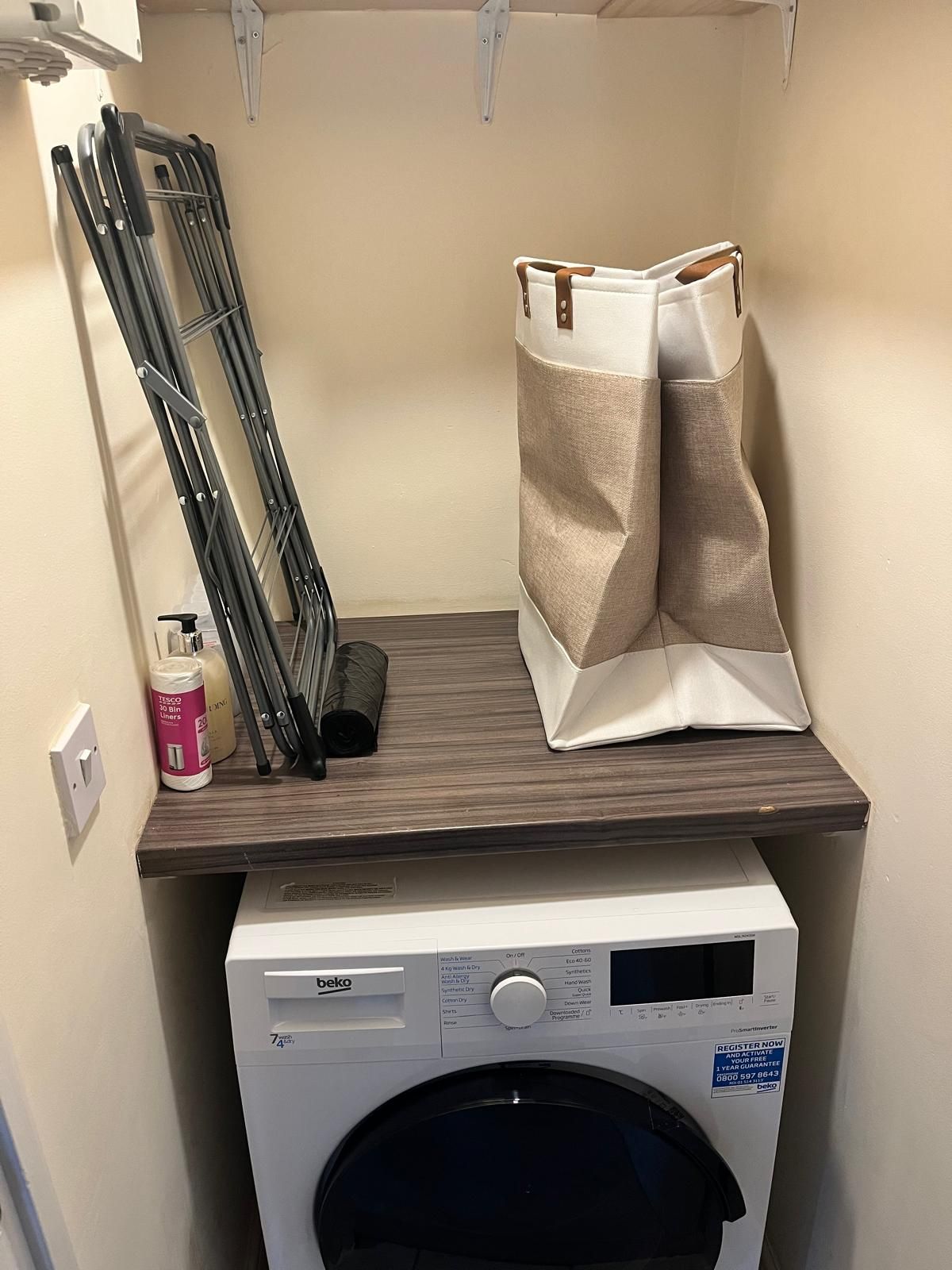Un área de lavandería con lavadora, tendedero y una bolsa de ropa.