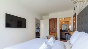 Hotellihuone, jossa on sänky, taulutelevisio, peilillä varustettu kylpyhuone ja ruokailutila.