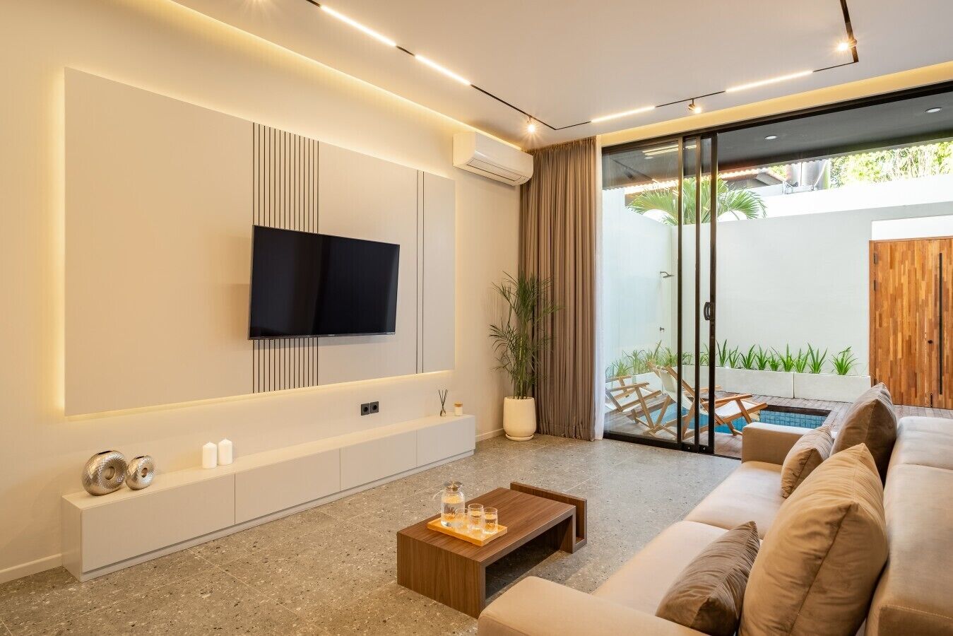 Ein modernes Wohnzimmer mit einem an der Wand befestigten Flachbildfernseher, einem Holztisch und einem beige farbenen Sofa.