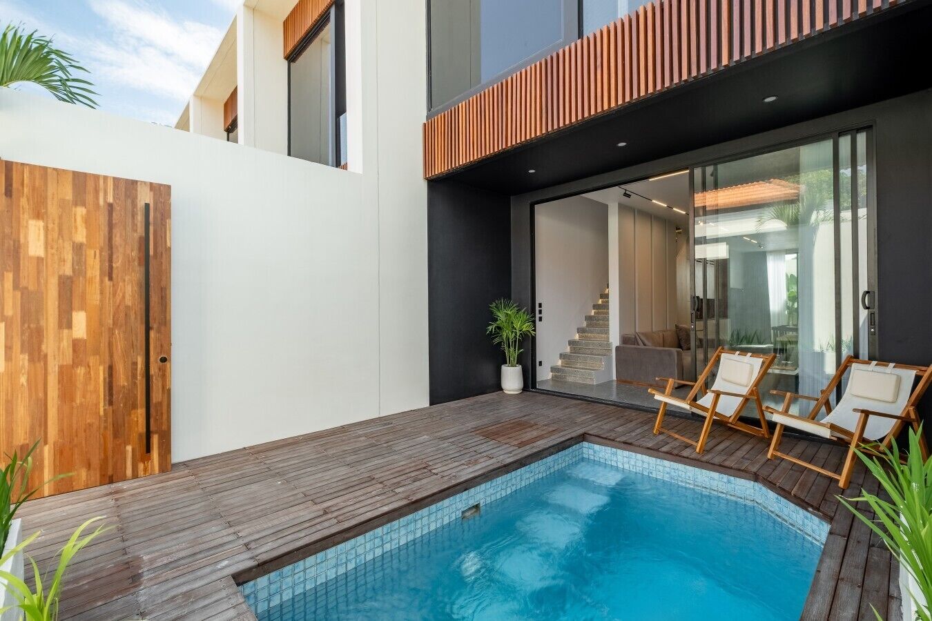 Un espace piscine extérieur moderne, doté d’une terrasse en bois, de chaises longues et d’un escalier menant à un espace intérieur.