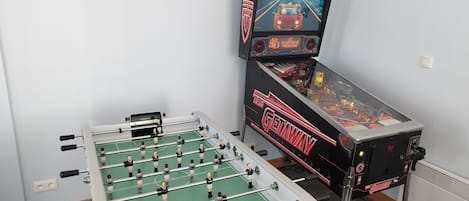 Una mesa de fútbol de mesa y una máquina de pinball en una habitación con paredes de colores claros.