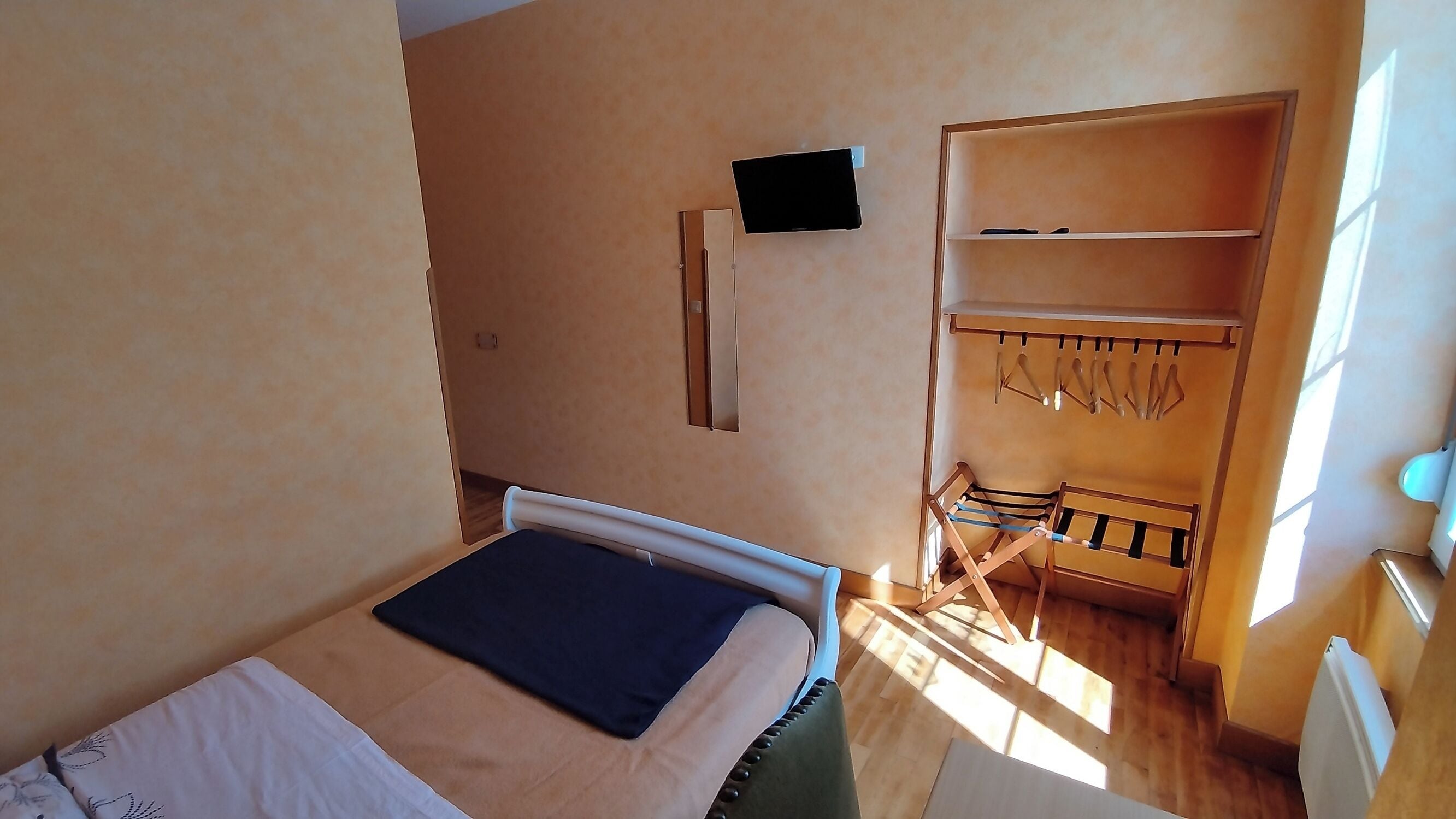 A bedroom with a bed, a wardrobe, and a small TV on the wall.