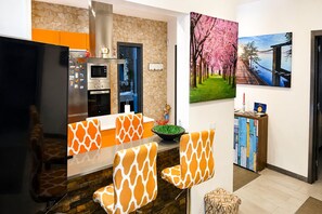 A modern kitchen with a stone backsplash, a built-in oven, and a microwave. There are two chairs with a giraffe pattern, a bowl of green vegetables, and a painting of cherry blossoms. - Holiday Home in Lajares for 5 (Lajares)