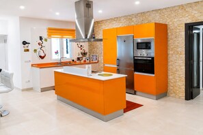 A modern kitchen with a central island, stainless steel appliances, and orange cabinetry. - Holiday Home in Lajares for 5 (Lajares)