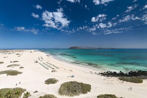 Een strand met helder turquoise water, wit zand en schaarse begroeiing.