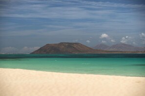A beach with clear turquoise water and a mountain in the background. - Holiday Home in Lajares for 5 (Lajares)