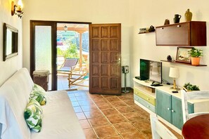 A room with a bed, a TV, a desk, and a door leading to an outdoor area with a chair and a table. - Holiday home in Fuencaliente for 3 (Fuencaliente, La Palma)