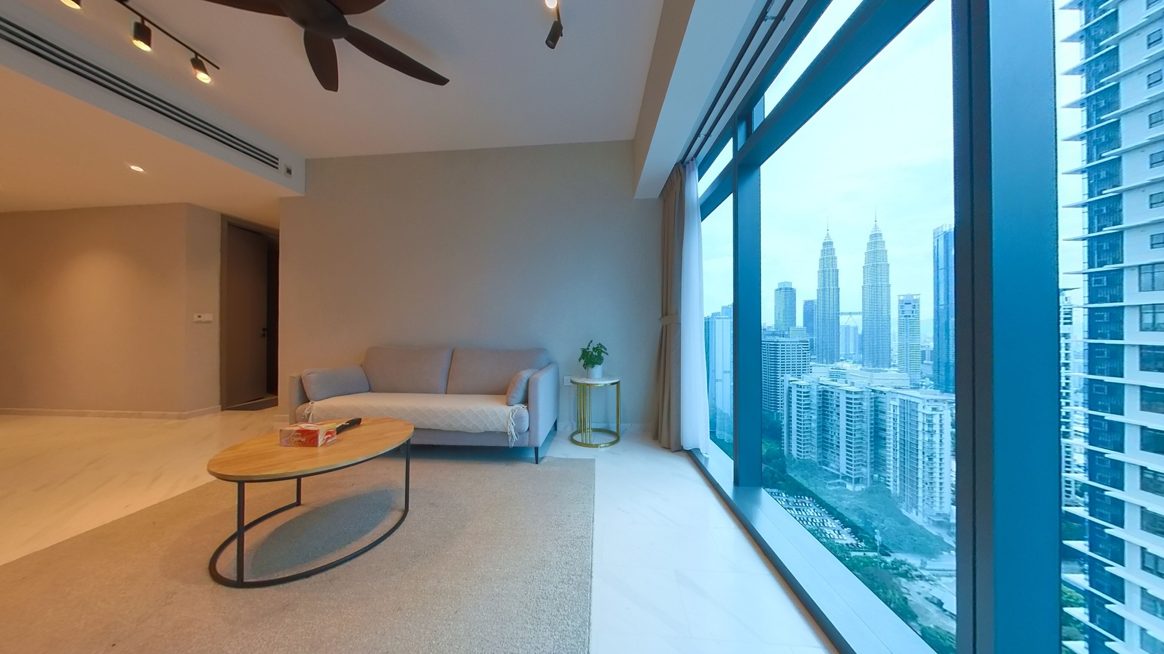 A modern living room with a sofa, a coffee table, and a view of a cityscape through large windows.