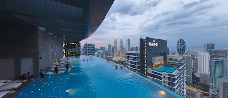 Ein Infinity-Pool mit Blick auf eine Stadtlandschaft, darunter die Petronas Towers, und ein Gebäude mit der Aufschrift 'The Manor'.