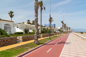 Eine Küstenstraße gesäumt von Palmen und Gebäuden, darunter ein weißes Gebäude mit Bogenfenstern und ein blaues Gebäude im Hintergrund.