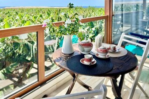 Une table placée devant un champ verdoyant, avec une carafe blanche, une théière, des tasses et des soucoupes.